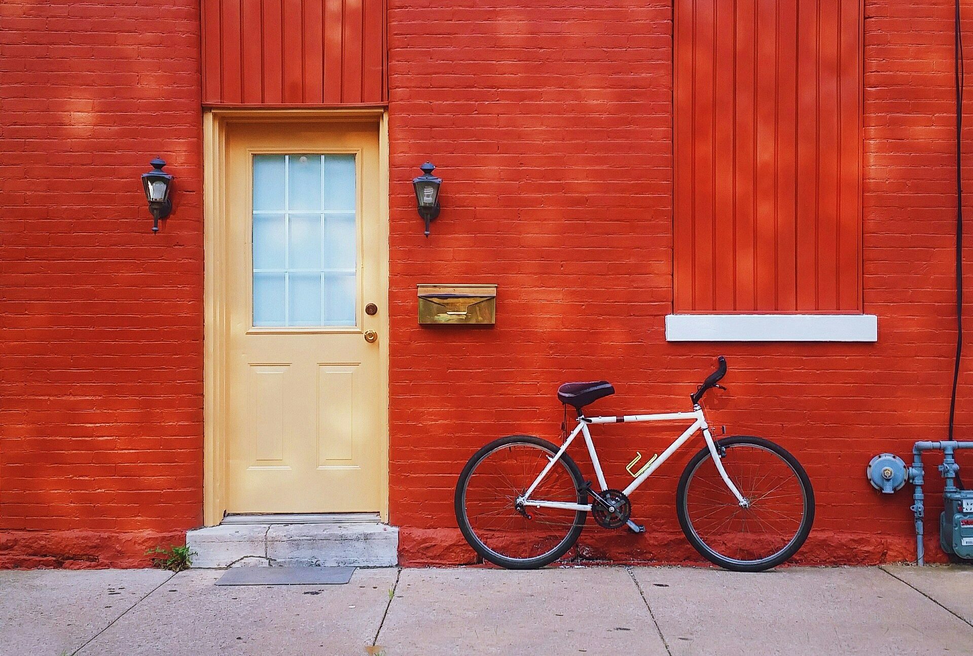 A bicycle stands ready for action, leaning against a cayenne-painted brick wall, just outside a cream-colored door. Where will its next adventure take it?